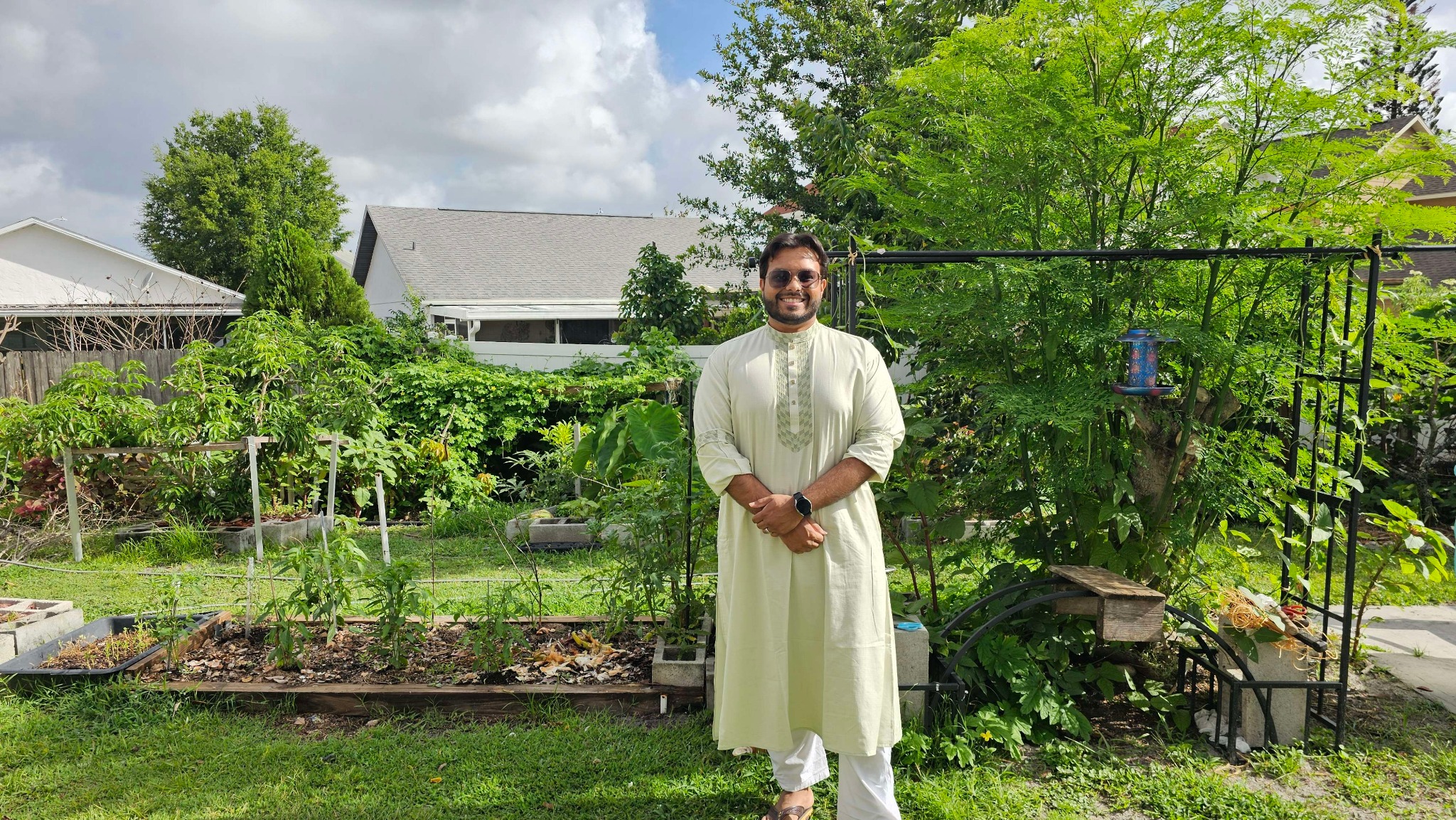 Siam standing among the plants and raised beds in his backyard garden